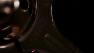 Metalik bir film makarasının yakın plan çekimi karanlık bir ortamda hızla dönüyor ve röfleler dönen kenarlara takılıyor.