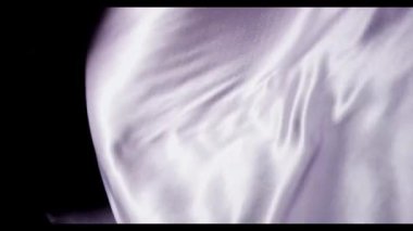 Lüks moda ve tekstil tasarımı için yavaş çekimde lavantalı kumaş sallanıyor ve zarif bir şekilde arka planda dalgalanıyor.