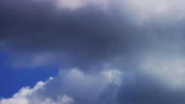 Beyaz kabarık bulutların üzerinde yuvarlanan büyük kara fırtına bulutları parlak mavi bir gökyüzü arka planına karşı dramatik bir hava değişimi etkisi yaratıyor.