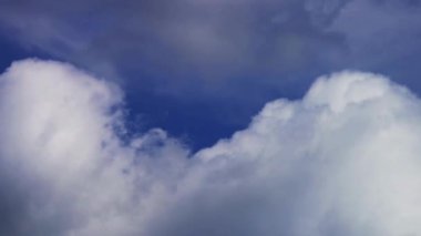 Kalın beyaz kümülüs bulutları mavi gökyüzünde dalgalanır ve hareket eder. Bu da doğal arka plan için ağır ve dokulu bir görünüm yaratır.