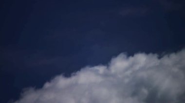 Pofuduk beyaz ve gri kümülüs bulutları açık ve aydınlık bir günde mavi bir arka planda yavaşça ilerliyorlar.