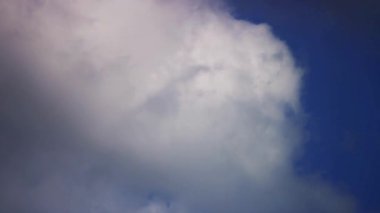 Parlak ve güneşli bir öğleden sonra, derin mavi gökyüzüne doğru hareket eden güzel, büyük, beyaz, kabarık bulutlar.