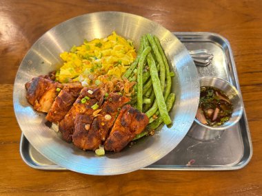 Tayland usulü tavuk, çırpılmış yumurta, uzun fasulye ve pilav. Ekşi sos ve tava tabağıyla ahşap masada servis edilen tipik bir Asya Tayland yemeği. Yemek fotoğrafçılığı