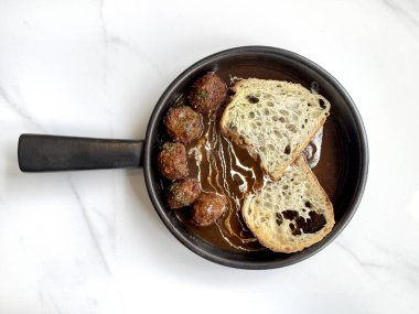 Klasik İtalyan usulü tavuk köftesi, stroganoff kremalı ve sarımsaklı ekmek. Otlar ve kekliklerle tatlandırılmış, seramik bir tavada servis edilmiş, beyaz mermer bir masada izole edilmiş..