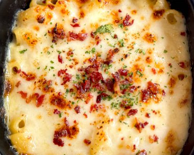 İçinde domuz pastırması ve risotto olan klasik İtalyan güveci. Üstünde erimiş mozarella peyniri var. Bitki ve soğanla tatlandırılmış, siyah bir tabakta servis edilmiş, beyaz mermer bir masada izole edilmiş..