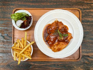 Salata ve kızarmış patates tabağıyla marine edilmiş parmesanlı tavuk yakın. Kırsal bir ahşap masada, beyaz bir tabakta servis edilmiş. Yemek fotoğrafçılığı