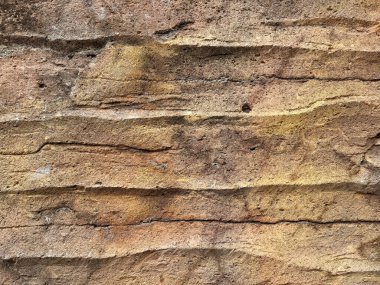 Duvara oyulmuş sert desenli doğal kahverengi uçurum taşına yakın çekim. Sert yatay damarları olan doğal kayrak taşı. Kusursuz arkaplan dokusu.