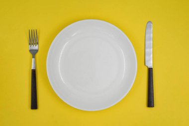 Masa ayarı, boş beyaz tabak, sarı arka planda çatal ve bıçak.
