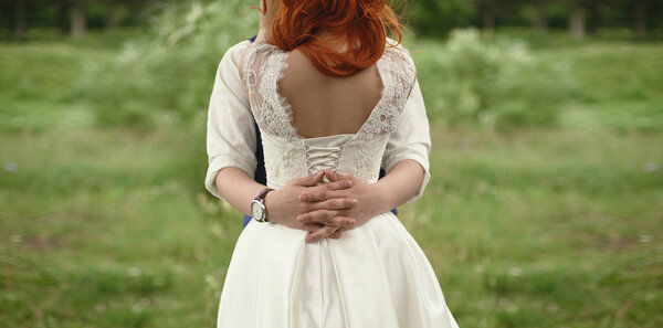 hands hugging the bride groom with red hair rear view in the green forest