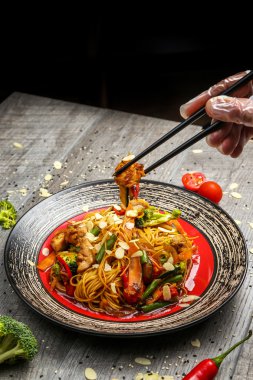 Siyah bir tabak üzerinde yemek çubukları ile ızgara tavuk ve sebze ile Erişte