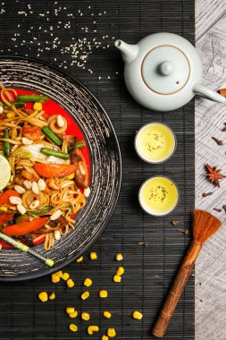 Siyah bir tabak üzerinde yemek çubukları ile ızgara tavuk ve sebze ile Erişte