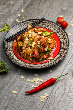 Siyah bir tabak üzerinde yemek çubukları ile ızgara tavuk ve sebze ile Erişte