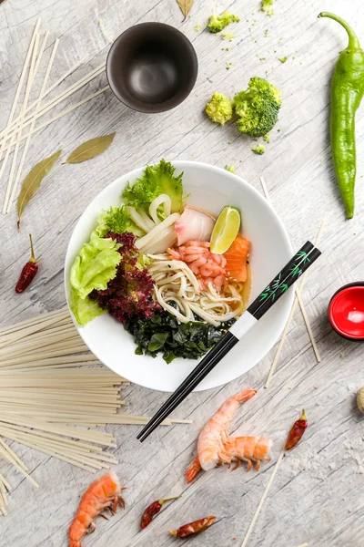 Deniz ürünleri, erişte ve beyaz bir tabakta sebze çorbası