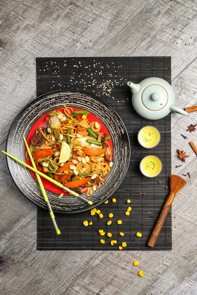 Nouilles au poulet grillé et légumes avec baguettes sur une assiette noire — Photo