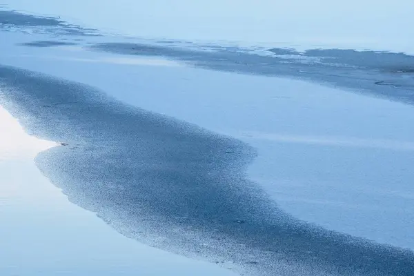 Kısmen donmuş gölet, mavi tonlarda soyut bir görüntü olarak gösterilir. 