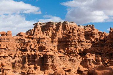 Mavi gökyüzünün altında tüylü beyaz bulutlarla olağanüstü sayıda cin oluşumları olan güzel bir kızıl kaya dağı. Güney Utah, ABD.