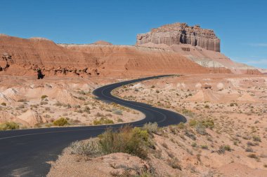 Goblin Vadisi Eyalet Parkı 'nda vahşi at Butte' a çıkan rüzgarlı bir asfalt yol. Gökyüzü açık mavi. Öndeki bitki örtüsü yol ile sınırdır. Güney Utah, ABD.