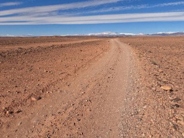 Çölde kirli bir yol Mavi gökyüzünün altında katmanlı bulutlarla
