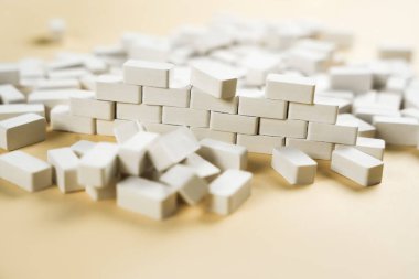 Sarı zemin üzerinde küçük bir duvar inşa edilmiş birçok beyaz minyatür tuğla yakın plan. Yaratıcı DIY kavramı