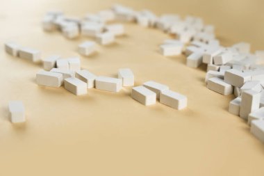 Açık bej bir yüzeyde çeşitli pozisyonlardaki küçük beyaz bloklar ilginç bir görsel ekran oluşturur. Bu bloklar, yaratıcılığı davet eden oyuncu ve sanatsal bir düzenleme olduğunu gösteriyor..