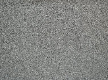 Kaba desenli gri beton bir duvar manzarası. Duvar kentsel bir çevrenin bir parçası. Güneş ışığı yüzeyde önemli noktalar yaratır.