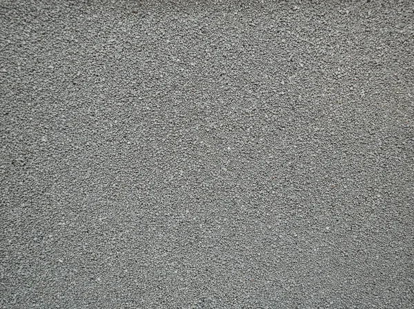 Kaba desenli gri beton bir duvar manzarası. Duvar kentsel bir çevrenin bir parçası. Güneş ışığı yüzeyde önemli noktalar yaratır.