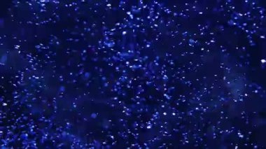 Havada kabarcıklar ve su damlacıkları yüzüyor. Mavi ışık güçlü bir kontrast yaratır. Bu, insanlarla dolu bir şehir ortamında bir akşam etkinliği sırasında gerçekleşir..