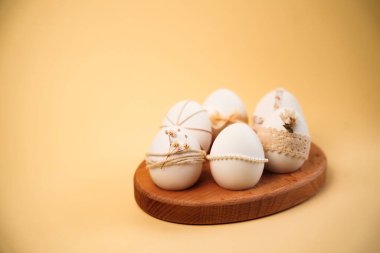 Paskalya yumurtaları ahşap bir tabakta düzenlenir. Her yumurtanın doğal malzemelerden yapılmış farklı dekorasyonları var. Ayar, yumurtaları ön plana çıkaran basit bir arkaplan içeriyor..