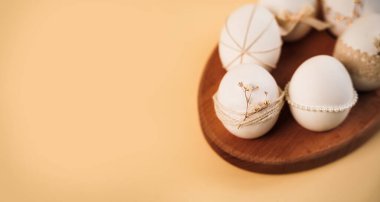 Paskalya boyunca yumurtalar basit tasarımlarla süslenir ve ahşap bir tabağa yerleştirilir. Işık arka planı renkleri ve yaratıcılığı vurgulayan neşeli bir hava katıyor..