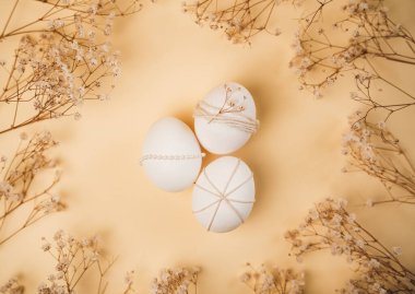 Paskalya yumurtaları sade bir arka planda düzenlenir. Her yumurta farklı malzemelerle süslenmiş. Kurumuş çiçekler yumurtaların etrafını sarar ve ekrana mevsimsel bir dokunuş ekler..
