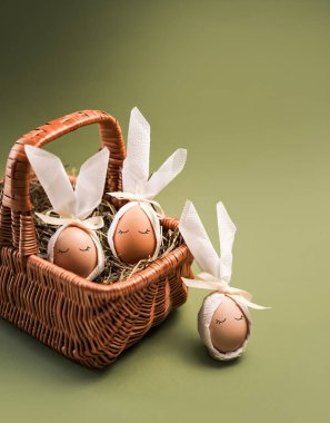Hasır bir sepette hazırlanmış Paskalya yumurtaları. Yumurtalar tavşan kulaklarına benzemesi için beyaz kumaşla süslenmiş. Yeşil arkaplan ile ayarlar basit.