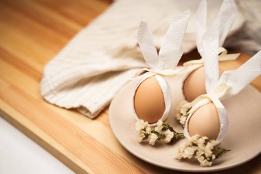 Paskalya yumurtaları dekoratif çiçek ve kumaş dokunuşlarıyla bir tabakta düzenlenir. Sahne, Paskalya bayramının ruhunu ve festival hazırlıklarını gösteriyor..