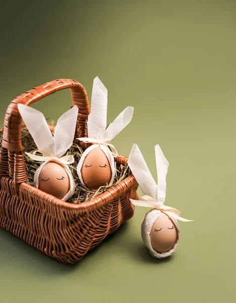 Hasır bir sepette hazırlanmış Paskalya yumurtaları. Yumurtalar tavşan kulaklarına benzemesi için beyaz kumaşla süslenmiş. Yeşil arkaplan ile ayarlar basit.