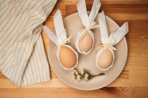 Üç yumurtadan oluşan bir set, kurdelelerle süslenmiş ve beyaz kumaşa sarılmış bir tabakta oturmaktadır. Küçük bir çiçek sahneye doğanın bir dokunuşunu ekler. Mutfakta sıcak bir hava var, Paskalya 'ya özgü..