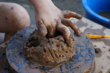 Küçük bir çocuğun elleri döner çarkın üzerindeki bir kil parçasını yoğurur ve şekillendirir, seramik bir ürün yaratır.