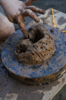 Küçük bir çocuğun elleri döner çarkın üzerindeki bir kil parçasını yoğurur ve şekillendirir, seramik bir ürün yaratır.