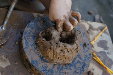 Küçük bir çocuğun elleri döner çarkın üzerindeki bir kil parçasını yoğurur ve şekillendirir, seramik bir ürün yaratır.