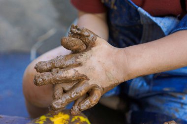 Küçük bir çocuğun elleri döner çarkın üzerindeki bir kil parçasını yoğurur ve şekillendirir.
