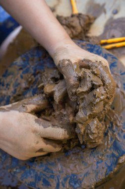 Küçük bir çocuğun elleri döner çarkın üzerindeki bir kil parçasını yoğurur ve şekillendirir.