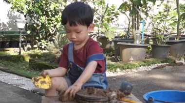 Dışarıda dönen tekerleğin üzerinde kille oynayan küçük bir çocuk. Çocuk oyununa dalmış, çocukluk keşfi sahnesi yaratıyor.