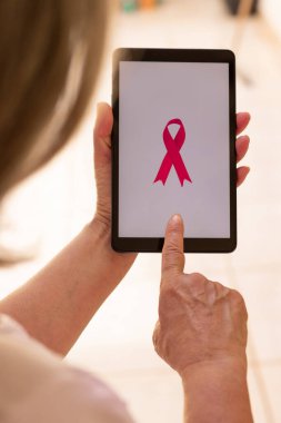 Elinde pembe kurdeleli tablet tutan olgun bir kadın. Teknoloji görüntülü Göğüs Kanseri Farkındalığı Ayı. 