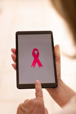 Elinde pembe kurdeleli tablet tutan olgun bir kadın. Teknoloji görüntülü Göğüs Kanseri Farkındalığı Ayı. 