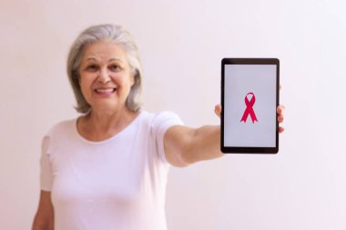 Elinde pembe kurdeleli tablet tutan olgun bir kadın. Teknoloji görüntülü Göğüs Kanseri Farkındalığı Ayı. 