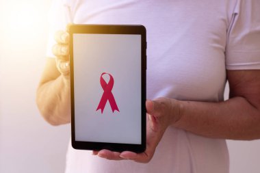 Elinde pembe kurdeleli tablet tutan olgun bir kadın. Teknoloji görüntülü Göğüs Kanseri Farkındalığı Ayı. 