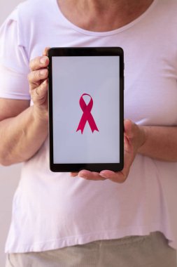 Elinde pembe kurdeleli tablet tutan olgun bir kadın. Teknoloji görüntülü Göğüs Kanseri Farkındalığı Ayı. 