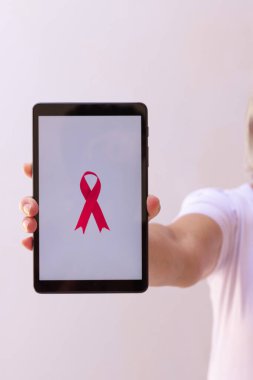 Elinde pembe kurdeleli tablet tutan olgun bir kadın. Teknoloji görüntülü Göğüs Kanseri Farkındalığı Ayı. 