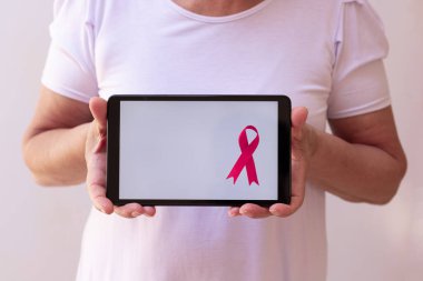 Elinde pembe kurdeleli tablet tutan olgun bir kadın. Teknoloji görüntülü Göğüs Kanseri Farkındalığı Ayı. 