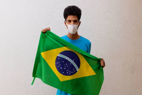 拿着一面挂在白色上的巴西国旗的戴着大面罩的黑人 — 图库照片