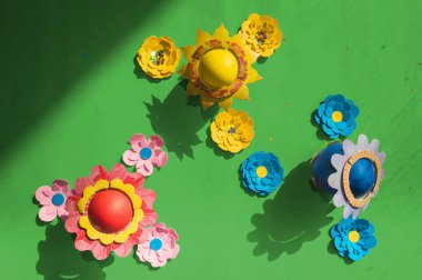 Çiçek şapkalı yumurtaların ve parlak yeşil arka planda kağıt çiçeklerin renkli Paskalya arkaplanı