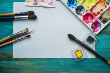 Yukarıdan, boya fırçaları, boyalar, kağıt ve palet gibi malzemeler yaratan suluboya resim çeşitleri üzerine görüş